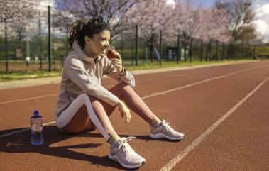 Cheerful young sportswoman eating an apple on running track.